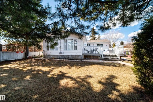 White siding residence featuring a spacious rear deck with stairs descending to a concrete pathway and a large lawn area - 10231 46 Street, Edmonton, AB - Outdoor