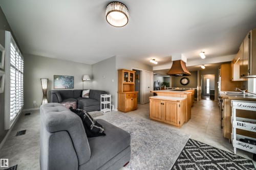 Open-concept living area featuring a kitchen with light wood cabinetry, a central island with integrated range, and a distinctive copper-toned range hood - 10231 46 Street, Edmonton, AB - Indoor