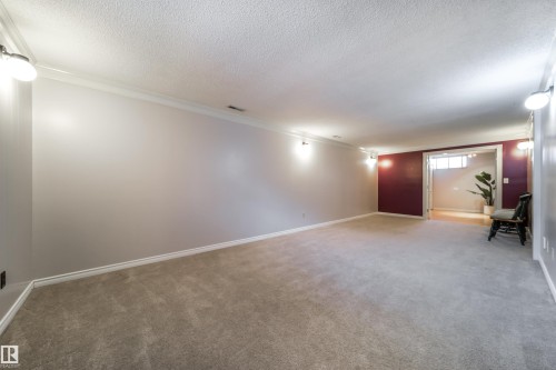 Spacious carpeted room featuring crown molding, baseboards, and wall-mounted lighting - 10231 46 Street, Edmonton, AB - Indoor Photo Showing Other Room