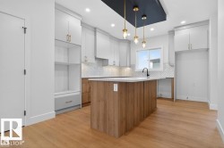Modern kitchen featuring a central island with wood-finish paneling, white countertop, and gold-toned pendant lighting - 