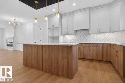 Kitchen featuring a large island with a light-colored countertop, two-tone cabinetry, a herringbone tile backsplash, and light wood-finish flooring - 