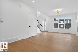 Spacious living area featuring wood-finish flooring, white walls, and a large multi-pane window - 