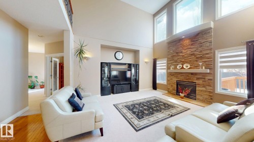 Spacious living area featuring high ceilings, large windows providing natural light, and a prominent stone fireplace - 613 Todd Link, Edmonton, AB - Indoor Photo Showing Living Room With Fireplace