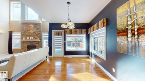Spacious living area featuring hardwood floors, a stone fireplace, and ample natural light from large windows - 613 Todd Link, Edmonton, AB - Indoor Photo Showing Other Room With Fireplace