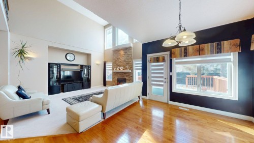 This inviting living space features hardwood flooring, a stone-faced fireplace, and large windows providing natural light - 613 Todd Link, Edmonton, AB - Indoor