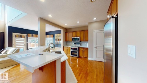 The kitchen features hardwood floors, light wood cabinetry, stainless steel appliances, and a central island with a sink and white countertop - 613 Todd Link, Edmonton, AB - Indoor Photo Showing Kitchen With Double Sink