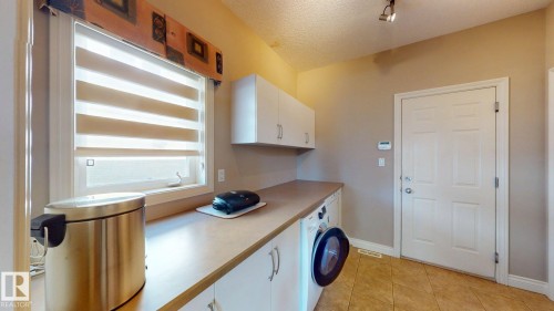The utility room features a window with blinds, a counter with cabinets, a washing machine, and tiled flooring - 613 Todd Link, Edmonton, AB - Indoor