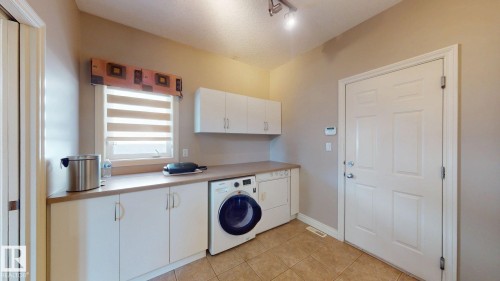 Laundry area featuring a window with blinds, white cabinetry, a front-loading washing machine, and a dryer - 613 Todd Link, Edmonton, AB - Indoor Photo Showing Laundry Room