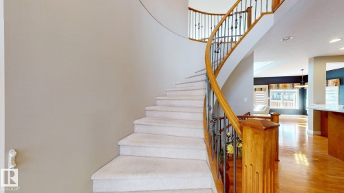 Elegant curved staircase with carpeted treads and a wooden handrail with decorative metal spindles - 613 Todd Link, Edmonton, AB - Indoor Photo Showing Other Room