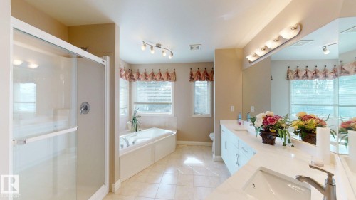 Bathroom featuring a glass-enclosed shower, a built-in bathtub, dual vanity sinks with a large mirror, and tiled flooring - 613 Todd Link, Edmonton, AB - Indoor Photo Showing Bathroom