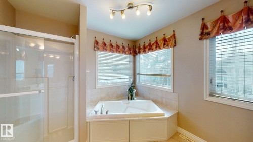 Bathroom featuring a built-in tub with surrounding tile, a glass-enclosed shower, and windows with blinds - 613 Todd Link, Edmonton, AB - Indoor Photo Showing Bathroom