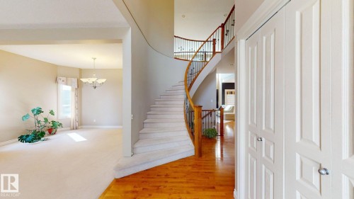 This property features a grand curved staircase with wood handrails and wrought iron balusters, a chandelier, and light-colored carpeting - 613 Todd Link, Edmonton, AB - Indoor Photo Showing Other Room