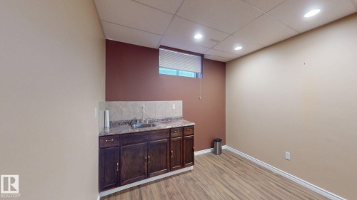 The property features a functional wet bar with a stainless steel sink, dark wood cabinetry, and a light-colored countertop with a tiled backsplash - 613 Todd Link, Edmonton, AB - Indoor