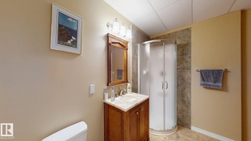Bathroom featuring a wooden vanity with a light-colored countertop and an integrated sink, a glass-enclosed shower with tiled walls, and light-colored walls and flooring - 613 Todd Link, Edmonton, AB - Indoor Photo Showing Bathroom