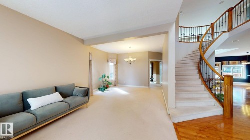 The property features an elegant curved staircase with wood and wrought iron railings, a spacious living area with light-colored carpeting, and hardwood flooring in the entrance - 613 Todd Link, Edmonton, AB - Indoor Photo Showing Other Room