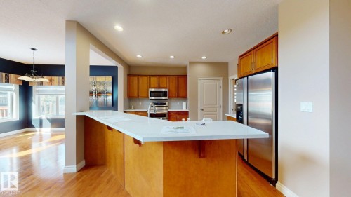 The kitchen features a large island with a light-colored countertop, wooden cabinetry, and stainless steel appliances, including a refrigerator and microwave - 613 Todd Link, Edmonton, AB - Indoor Photo Showing Kitchen With Upgraded Kitchen