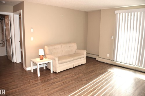 Living area featuring wood-finish flooring, neutral wall tones, and vertical blinds on the sliding glass door - 103 920 156 Street Nw, Edmonton, AB - Indoor Photo Showing Other Room
