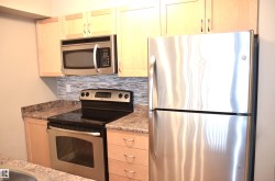 Kitchen with wood-finish cabinetry, stainless steel appliances, speckled countertops, and a mosaic tile backsplash - 