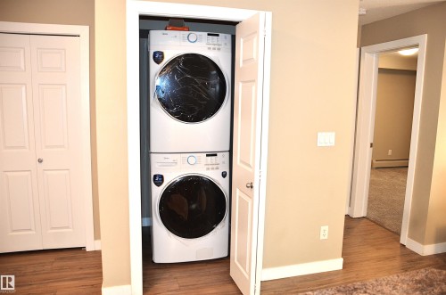 Dedicated laundry closet featuring a stacked washer and dryer, wood-finish flooring, and neutral wall paint - 103 920 156 Street Nw, Edmonton, AB - Indoor Photo Showing Laundry Room