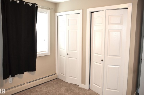 Interior room featuring two paneled bi-fold closet doors, a single window with white trim, and light brown carpeting - 103 920 156 Street Nw, Edmonton, AB - Indoor Photo Showing Other Room