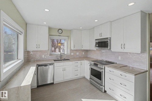 Modern kitchen featuring white cabinetry, stainless steel appliances, light-toned countertops, a tile backsplash, and recessed lighting - 3903 32 Street, Edmonton, AB - Indoor Photo Showing Kitchen With Upgraded Kitchen