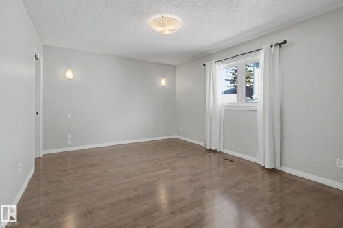 Spacious room featuring wood-finish flooring, light grey walls, and a large window - 3903 32 Street, Edmonton, AB - Indoor Photo Showing Other Room