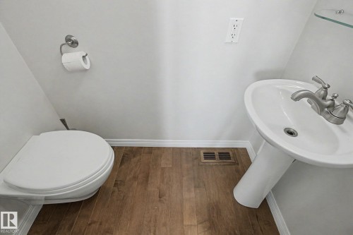 Powder room featuring wood-finish flooring, a white pedestal sink with brushed nickel faucet, and a white toilet - 3903 32 Street, Edmonton, AB - Indoor Photo Showing Bathroom