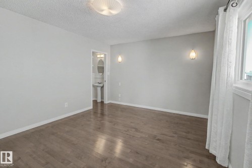 Spacious room featuring wood-finish flooring, a contemporary ceiling light fixture, and two wall sconces - 3903 32 Street, Edmonton, AB - Indoor Photo Showing Other Room