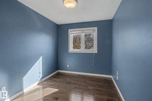 Room featuring wood-finish flooring, blue painted walls, a white trim window, and a flush-mount ceiling light - 3903 32 Street, Edmonton, AB - Indoor Photo Showing Other Room