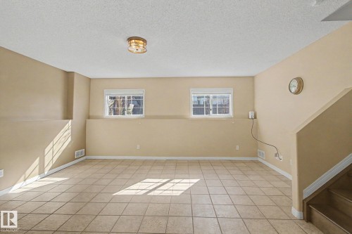 Spacious room featuring neutral tone walls, tile flooring, two windows, recessed lighting, and a visible staircase - 3903 32 Street, Edmonton, AB - Indoor Photo Showing Other Room