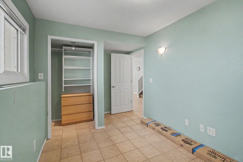 Room featuring light green wall paint, tile flooring, a window with white blinds, a built-in closet system with shelving and drawers, and a white interior door - 3903 32 Street, Edmonton, AB - Indoor Photo Showing Other Room
