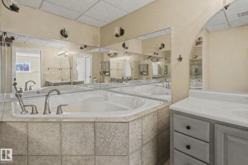 Corner soaking tub with tile surround, brushed nickel fixtures, a vanity with dual sinks, and extensive wall-mounted mirrors - 3903 32 Street, Edmonton, AB - Indoor