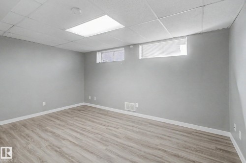 Spacious room featuring light gray walls, wood-finish flooring, white baseboards, and a white acoustical tile ceiling - 3903 32 Street, Edmonton, AB - Indoor