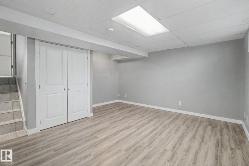 Spacious room featuring wood-finish flooring, light grey painted walls, white bi-fold doors, and a drop ceiling with recessed lighting - 3903 32 Street, Edmonton, AB - Indoor Photo Showing Other Room