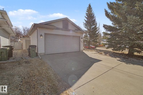 Attached garage with a wide concrete driveway, featuring white siding, a single garage door, and an exterior light fixture - 3903 32 Street, Edmonton, AB - Outdoor