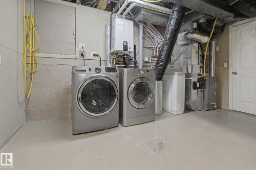 Dedicated laundry area featuring a front-loading washer and dryer, concrete flooring, and exposed utility lines - 3903 32 Street, Edmonton, AB - Indoor Photo Showing Laundry Room