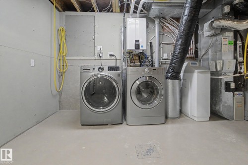 Utility area featuring concrete flooring, exposed ceiling joists, two front-loading laundry machines, a water heater, and a water softener system - 3903 32 Street, Edmonton, AB - Indoor Photo Showing Laundry Room