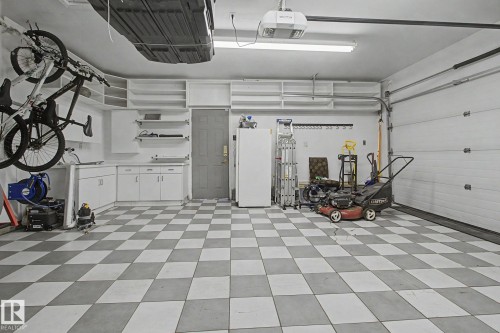 Spacious garage featuring checkerboard floor tiling, extensive built-in cabinetry, overhead shelving, and a panel garage door - 3903 32 Street, Edmonton, AB - Indoor Photo Showing Garage