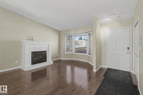 Living area featuring wood-finish flooring, a white fireplace with an intricate tile surround, and a bay window - 3903 32 Street, Edmonton, AB - Indoor Photo Showing Living Room With Fireplace