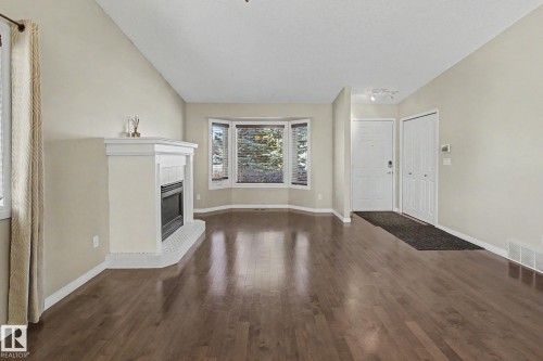 Spacious room featuring rich wood-finish flooring, a white mantel fireplace with tile surround, and a bay window - 3903 32 Street, Edmonton, AB - Indoor With Fireplace