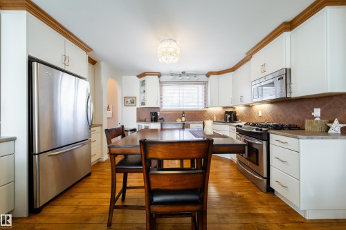 Kitchen featuring white cabinetry with wood crown molding, stainless steel appliances, wood-finish flooring, and a tiled backsplash - 8932 154 Street, Edmonton, AB - Indoor Photo Showing Kitchen
