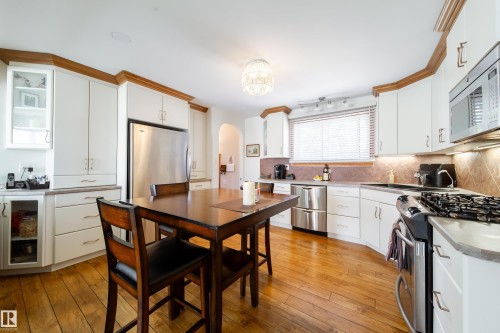 Kitchen featuring wood-finish flooring, white cabinetry with wood crown molding, stainless steel appliances, a tiled backsplash, and recessed lighting - 8932 154 Street, Edmonton, AB - Indoor Photo Showing Kitchen