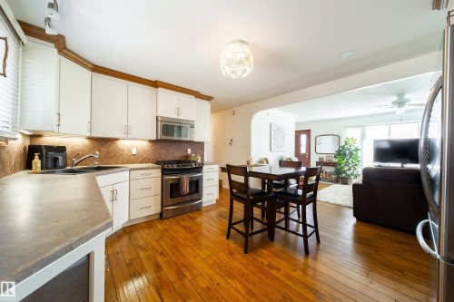Kitchen featuring wood-finish flooring, white cabinetry with wood trim, stainless steel appliances, and a tiled backsplash - 8932 154 Street, Edmonton, AB - Indoor