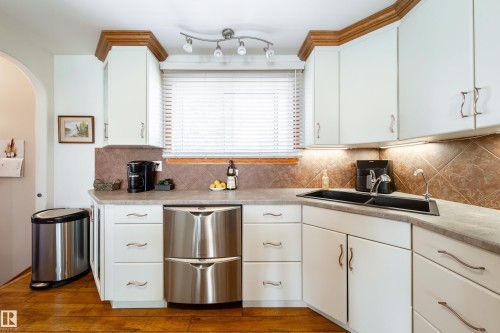 Kitchen featuring white cabinetry with wood crown molding, a tiled backsplash, and under-cabinet lighting - 8932 154 Street, Edmonton, AB - Indoor Photo Showing Kitchen With Double Sink