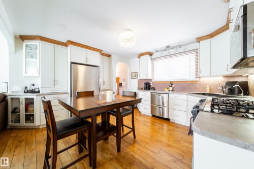 Bright kitchen featuring white cabinetry with wood-finish trim, stainless steel appliances, and wood-finish flooring - 8932 154 Street, Edmonton, AB - Indoor
