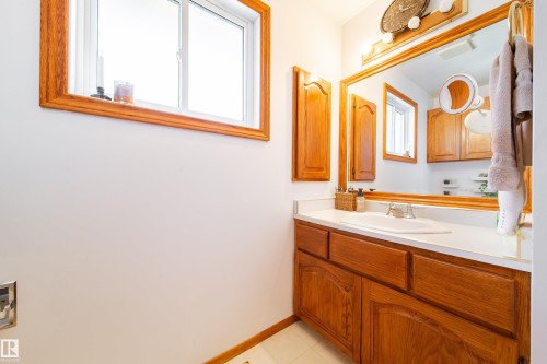 Bathroom vanity featuring wood-finish cabinetry with decorative arch panels, a single basin sink, and a white countertop - 8932 154 Street, Edmonton, AB - Indoor Photo Showing Bathroom