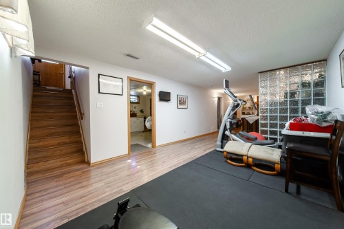 Finished lower level with wood-finish flooring, a glass block partition, and an open doorway to an additional room - 8932 154 Street, Edmonton, AB - Indoor
