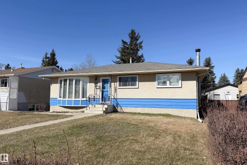 Bungalow exterior featuring a prominent bay window, stucco siding with a blue horizontal accent, and a front entry with wrought iron railings - 8932 154 Street, Edmonton, AB - Outdoor