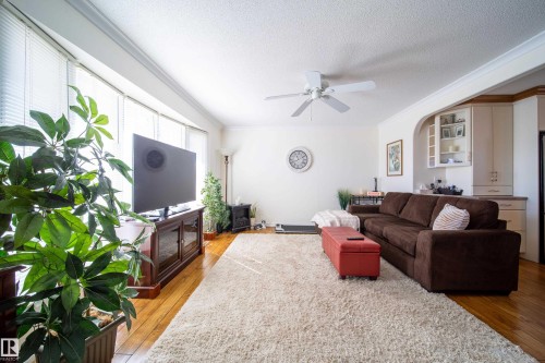 Living area featuring wood-finish flooring, a curved bay window, ceiling fan, crown molding, and built-in cabinetry with an archway - 8932 154 Street, Edmonton, AB - Indoor Photo Showing Living Room