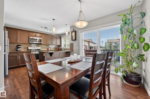Open-concept dining area featuring wood-finish flooring, a contemporary overhead light fixture, and a sliding glass door to a balcony - 1786 Cunningham Way Sw, Edmonton, AB - Indoor Photo Showing Other Room
